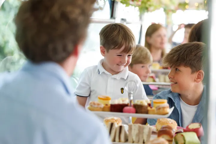 Children smiling and enjoying afternoon tea with pastries and sandwiches.