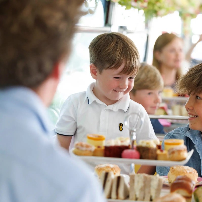 Children smiling and enjoying afternoon tea with pastries and sandwiches.