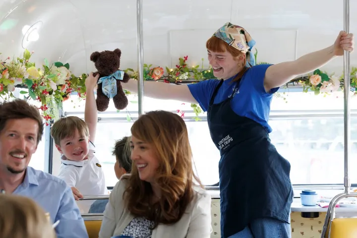 Woman in apron smiling on a bus with flowers, boy holding a teddy bear.