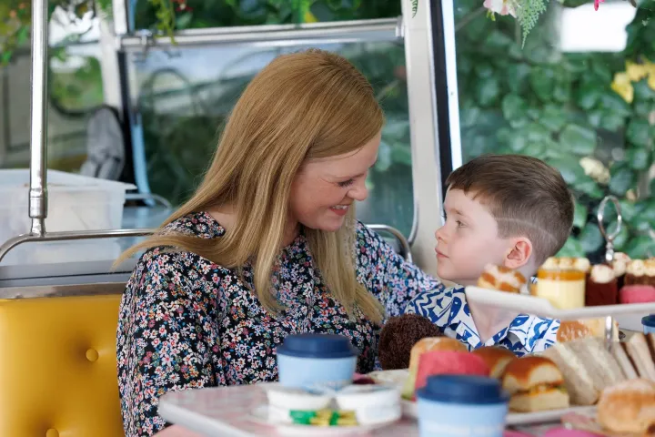 Woman and child smiling at each other in a cafe with food on the table.