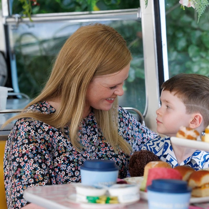 Woman and child smiling at each other in a cafe with food on the table.