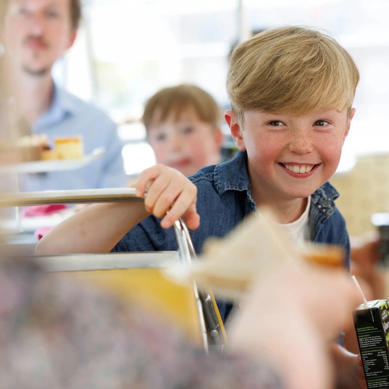 Smiling child holding a drink carton on a bus with people.