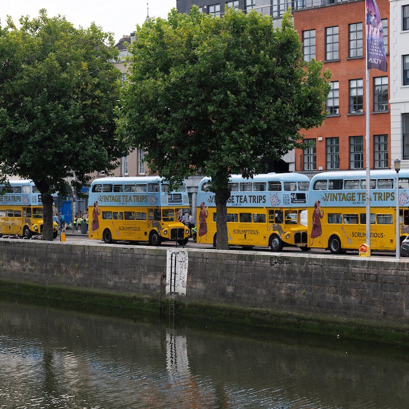 Row of vintage double-decker buses driving up the quays of the River Liffey