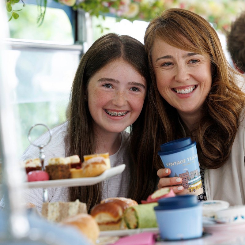 Mother and daughter enjoying afternoon tea with sandwiches and pastries on a table.