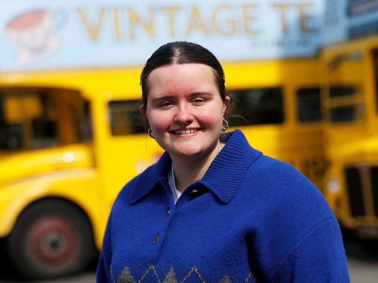 Nicole customer experience manager in blue sweater with yellow bus in background